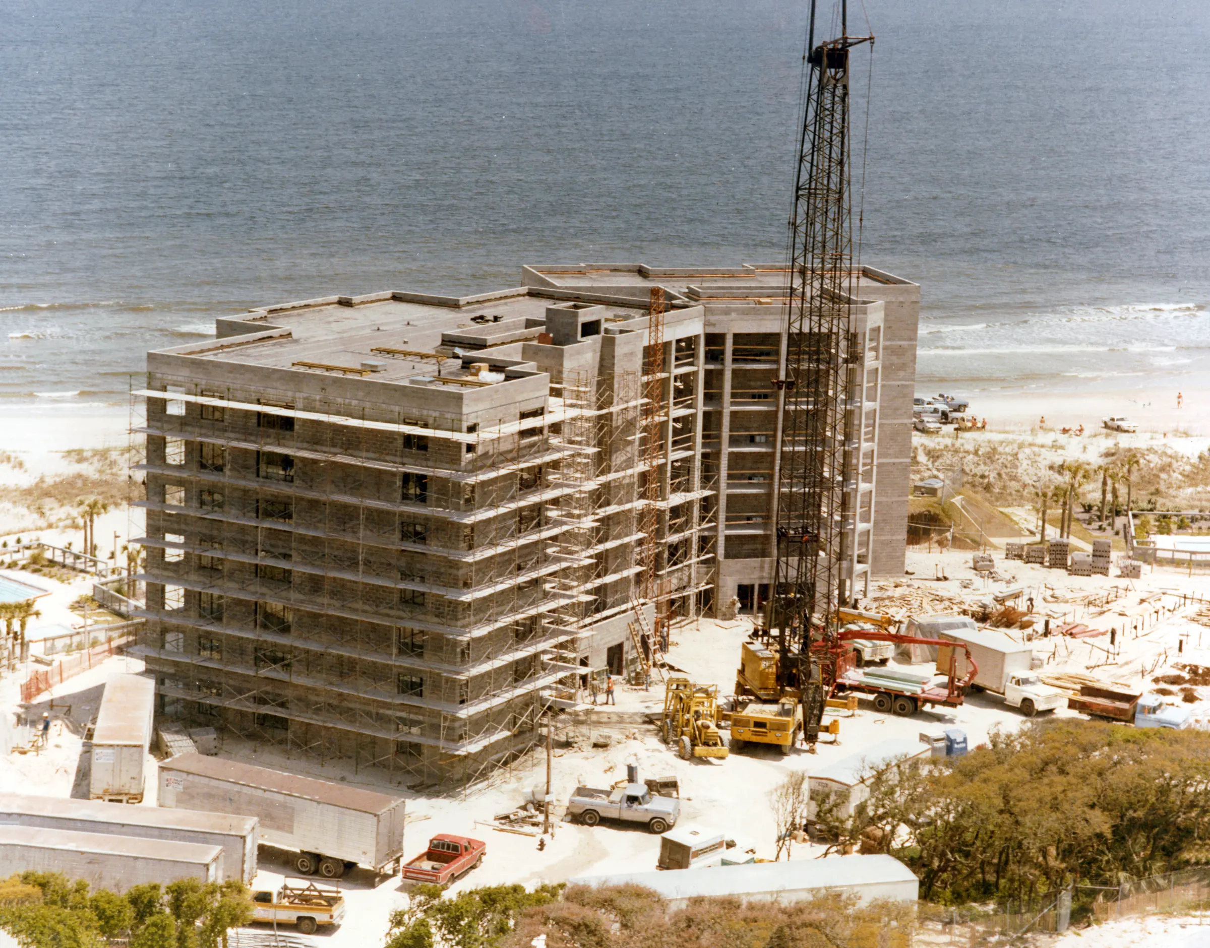 A seven-story building wrapped in scaffolding, with a tall crane beside it and the Atlantic Ocean behind